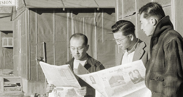 Roy Takeno and others reading the Manzanar Free Press in front of the office, 1943, photo by Ansel Adams, credit Library of Congress Prints & Photographs Division