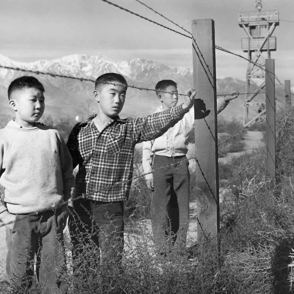 Three boys behind barbed wire, Manzanar, 1944. Photo by Toyo Miyatake.
