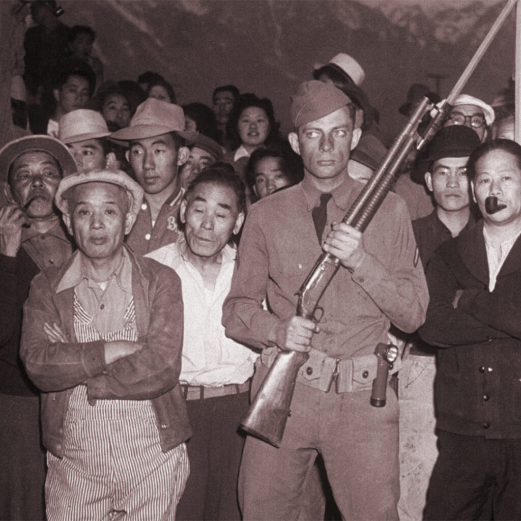 A guard with rifle with Japanese Americans who arrived at Manzanar, c1942