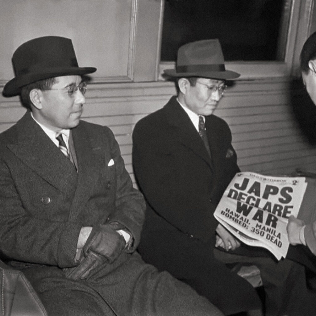 Two men reading the headline “Japs Declare War” while being transported to Ellis Island in federal custody, only hours after the attack on Pearl Harbor. December 7, 1941
